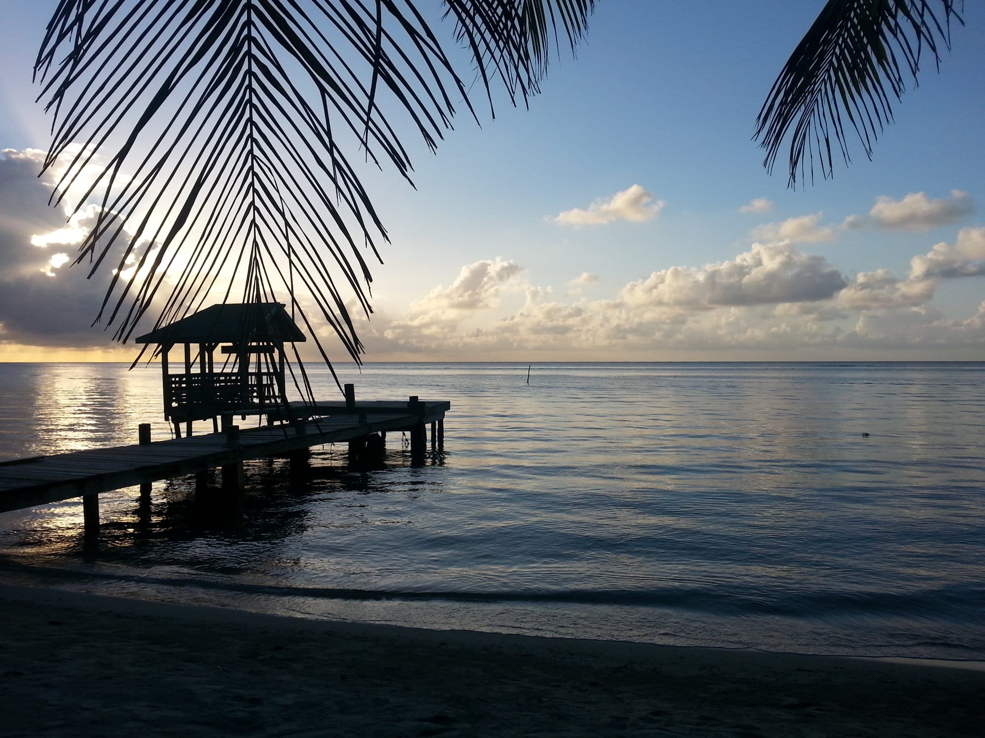 A wooden jetty in Honduras leading to the sea, including a small hut on it.